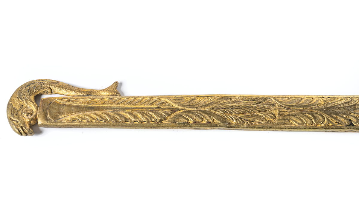 Stickert, oslipad klinga av plattoval form, handtag av ebenholtz beslaget med förgylld ciselerad mässing med manshuvud. Parerstång med två djurhuvuden. Balja av förgylld mönstrad mässing med lilla riksvapnet. En ring saknas.