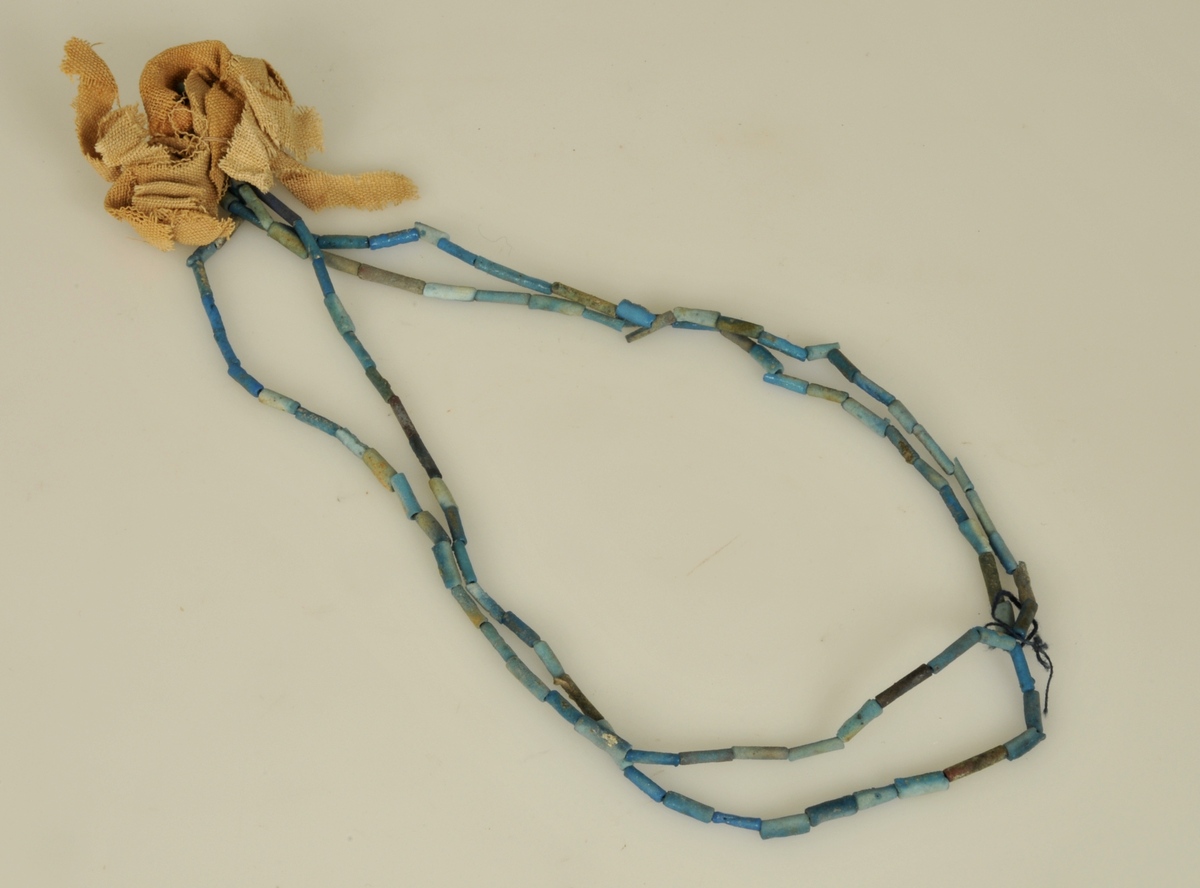 Gravfynd.

6 st. halsband av turkosfärgade fajanspärlor.
Tre av dem har vidhängande textila rester i form av linne-
remsor hopsatta till tofsar. Två naturfärgade, en röd.
Fyra av halsbanden har fastsatta fajansfigurer: 
en scarabé, två faraofigurer och en apgud.

Har tillhört de Adelsköldska samlingarna.
