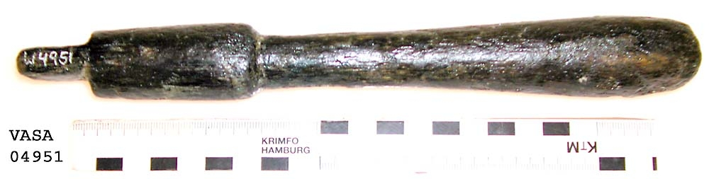 Svarvat skaft till mindre klubba. Ansatsen har ett kvadratiskt tvärsnitt. Ett hörn av ansatsen är avslagen i övrigt är skaftet helt intakt. Under ansatsen finns ett cylindriskt parti, vilket avslutas med en dekorrand. Därefter är skaftet koniskt och vidgar sig nedtill, för att i änden avslutas i en rundning. Vid ansatsen finns rester av grön korrosion.

För mer information se Dokumentationsblankett under Referenser – Länkade filer.