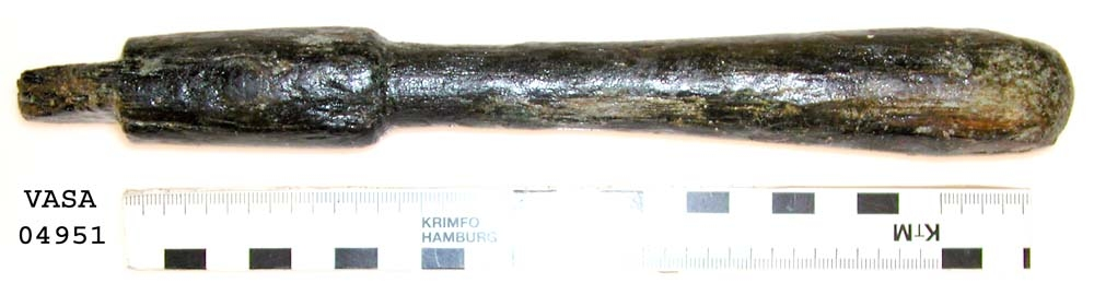 Svarvat skaft till mindre klubba. Ansatsen har ett kvadratiskt tvärsnitt. Ett hörn av ansatsen är avslagen i övrigt är skaftet helt intakt. Under ansatsen finns ett cylindriskt parti, vilket avslutas med en dekorrand. Därefter är skaftet koniskt och vidgar sig nedtill, för att i änden avslutas i en rundning. Vid ansatsen finns rester av grön korrosion.

För mer information se Dokumentationsblankett under Referenser – Länkade filer.