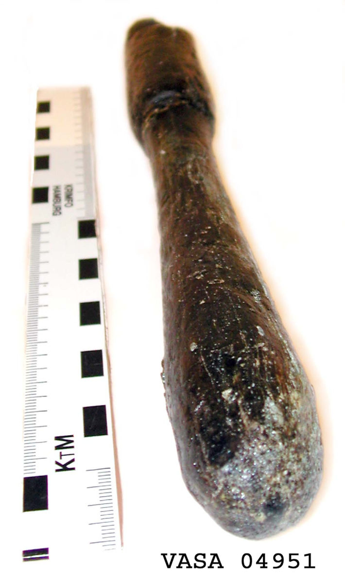 Svarvat skaft till mindre klubba. Ansatsen har ett kvadratiskt tvärsnitt. Ett hörn av ansatsen är avslagen i övrigt är skaftet helt intakt. Under ansatsen finns ett cylindriskt parti, vilket avslutas med en dekorrand. Därefter är skaftet koniskt och vidgar sig nedtill, för att i änden avslutas i en rundning. Vid ansatsen finns rester av grön korrosion.

För mer information se Dokumentationsblankett under Referenser – Länkade filer.