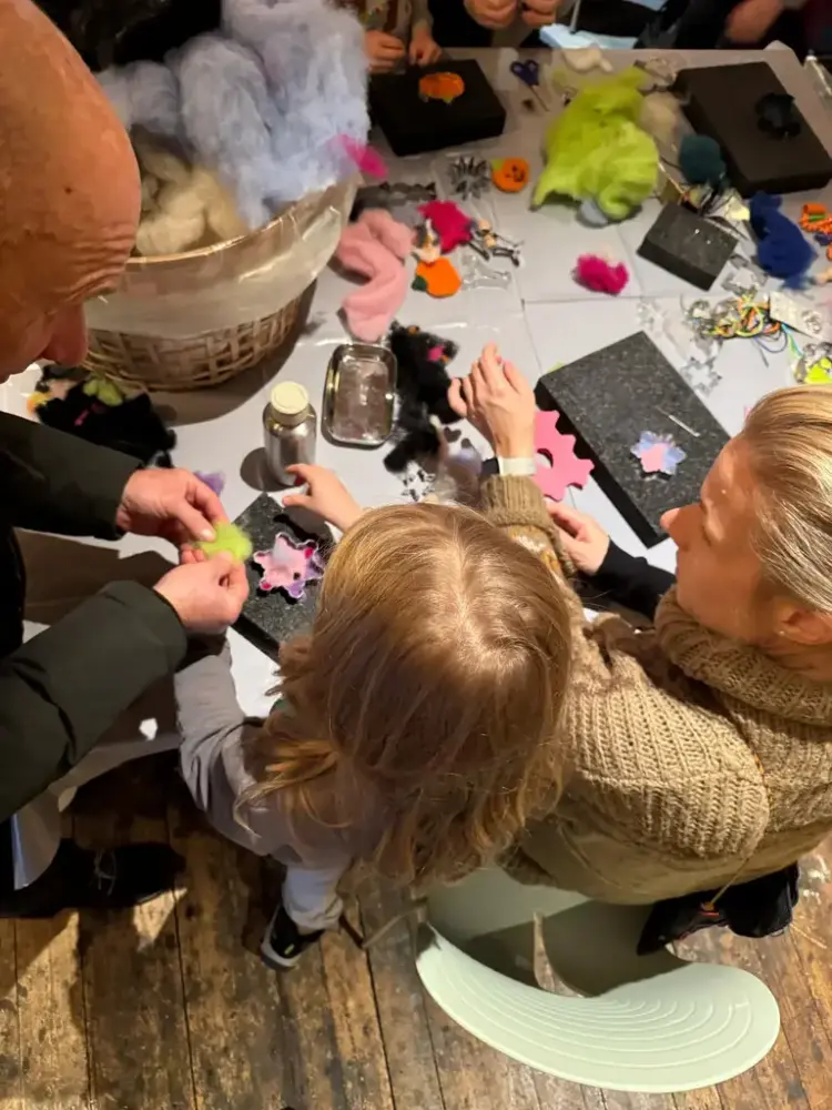 Her ser vi flere voksne og barn sammen rundt et bord, hvor de koser seg med nålefilting i pepperkakeformer