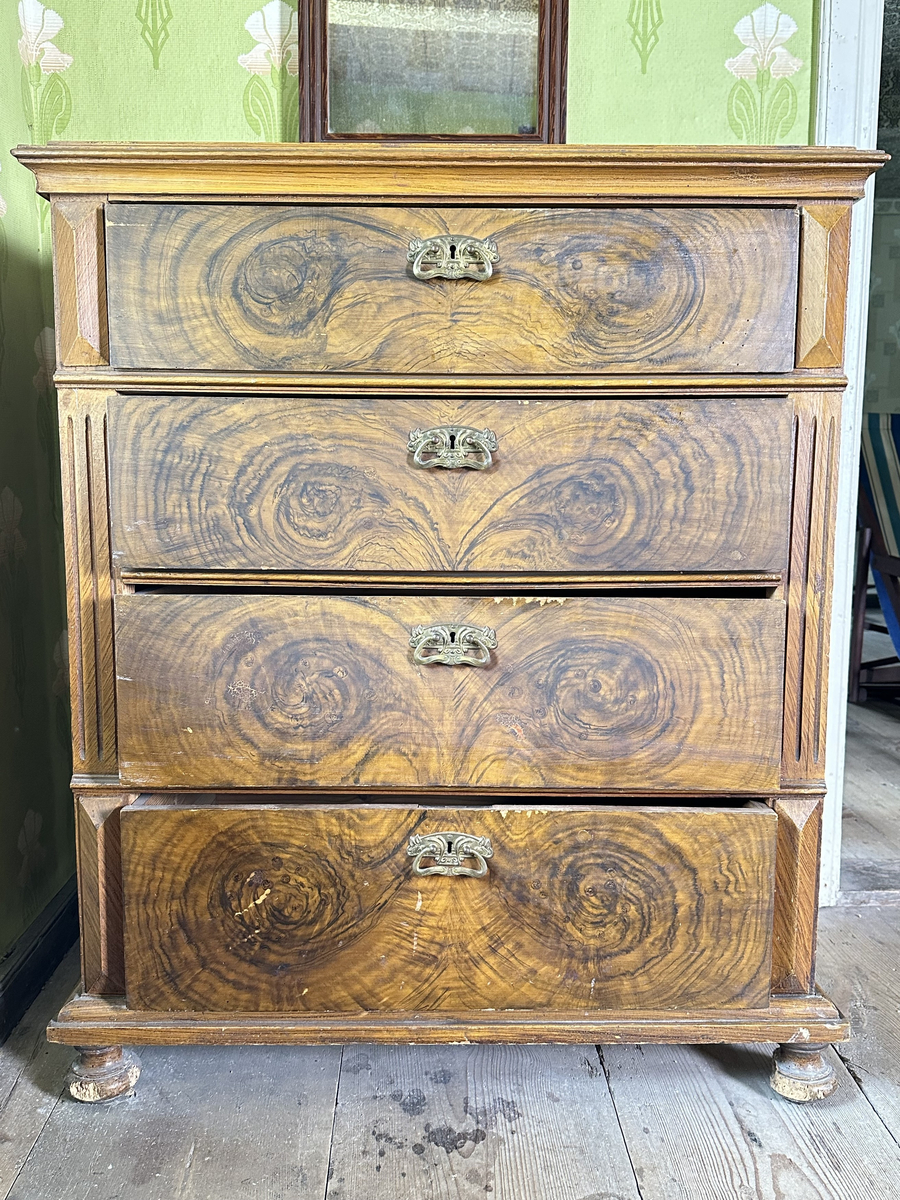 Byrå, av trä. Ådringsmålat i brunt. Profilerad kantig list upptill och nedtill. Svarvade fötter fram, fyrkantiga baktill. Fyra lådor. På ömse sidor av lådorna, fält med skurna prismor samt fält med kannelyrer. Beslag i gulmetall.