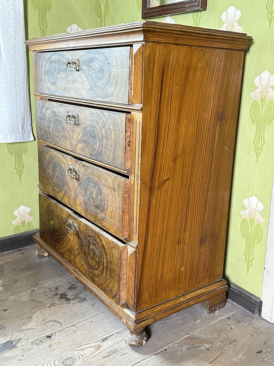 Byrå, av trä. Ådringsmålat i brunt. Profilerad kantig list upptill och nedtill. Svarvade fötter fram, fyrkantiga baktill. Fyra lådor. På ömse sidor av lådorna, fält med skurna prismor samt fält med kannelyrer. Beslag i gulmetall.