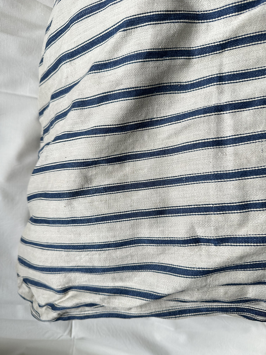 Bolster av linne med satinbindning. Gråvitt med ränder i blått. Hopsytt på tvären. Fyllt. Lappat.