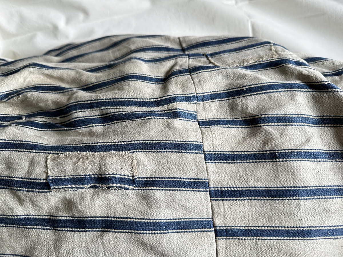 Bolster av linne med satinbindning. Gråvitt med ränder i blått. Hopsytt på tvären. Fyllt. Lappat.