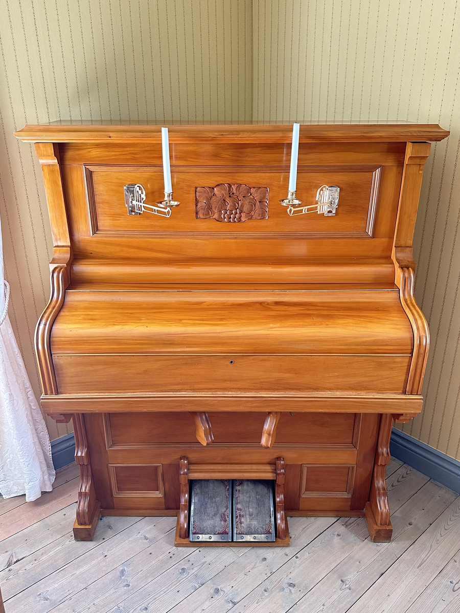 Harmonium i lackat trä. Plant krön, profilerad gavelframkant. Spegel med två dekorativa ljushållare i mässing samt trädekor i form av bär och blad. 14 andrag. Låsbart lock. Klädda trampor i metall. 