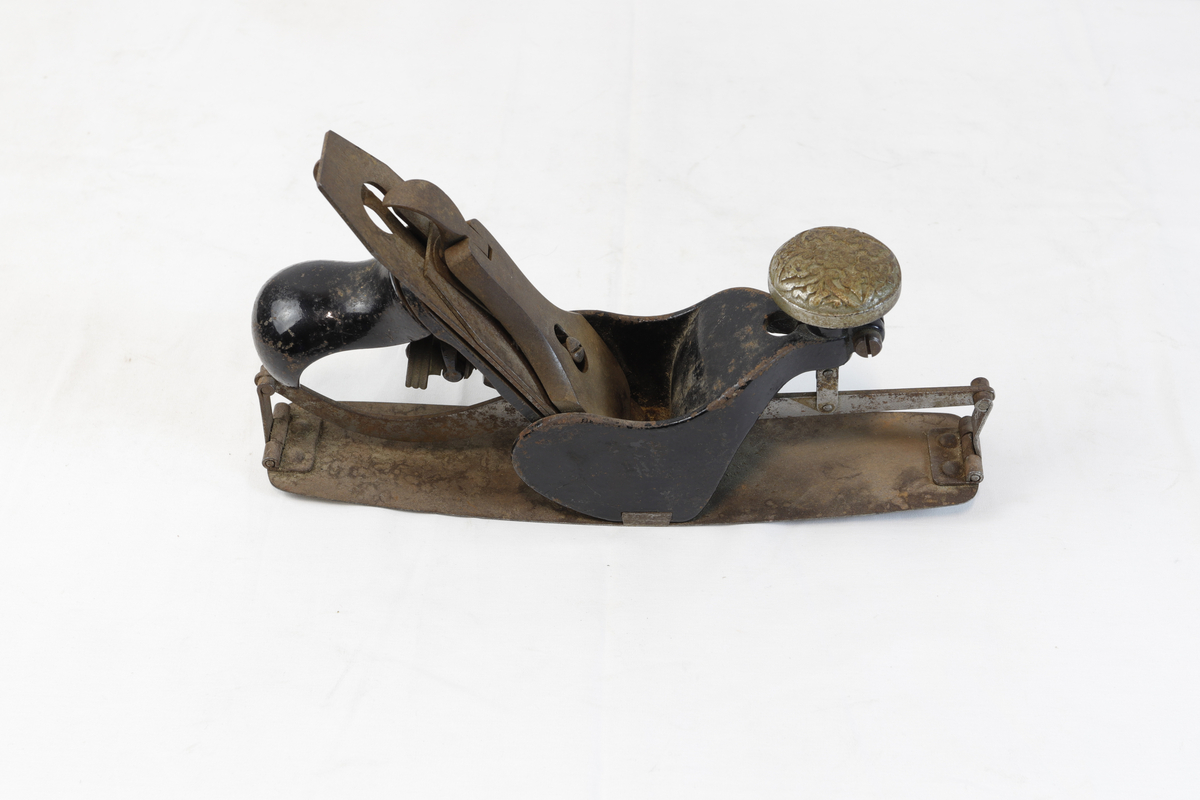 Justerbar buehøvel i metall. Håndtaket foran er dekorert med blomsterornamentikk. 
