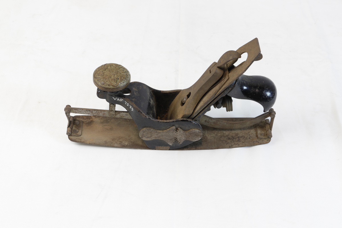 Justerbar buehøvel i metall. Håndtaket foran er dekorert med blomsterornamentikk. 
