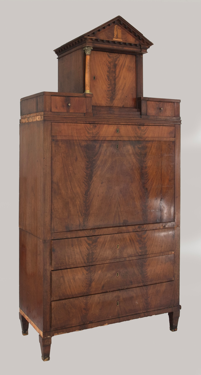 Skatoll i mahognifinér på tre. Nederst en skuffeseksjon med tre skuffer. Midtpartiet har skriveklaff, to skap og skuffer. Skapdørene viser intarsiamotiv forestillende kvinne ved søyle. På hver side av de to skapene er det marmorsøyler med forgylte bronsekapitler som dekker forsiden av smale, høye skuffer. Lave skuffer over og under skapene. Mellom skapene er det en åpning med speil og innlagt bunn. Øvre del av skatollen har et skap og to skuffer, en på hver side av skapet, med søyler av tre på hver side av skapdøren. Skatollen avsluttes med en gavl. Gavlfeltet har samme motiv som skapdørene i midtpartiet. Lave pyramideformete ben.