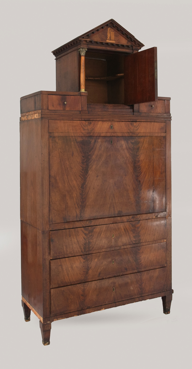 Skatoll i mahognifinér på tre. Nederst en skuffeseksjon med tre skuffer. Midtpartiet har skriveklaff, to skap og skuffer. Skapdørene viser intarsiamotiv forestillende kvinne ved søyle. På hver side av de to skapene er det marmorsøyler med forgylte bronsekapitler som dekker forsiden av smale, høye skuffer. Lave skuffer over og under skapene. Mellom skapene er det en åpning med speil og innlagt bunn. Øvre del av skatollen har et skap og to skuffer, en på hver side av skapet, med søyler av tre på hver side av skapdøren. Skatollen avsluttes med en gavl. Gavlfeltet har samme motiv som skapdørene i midtpartiet. Lave pyramideformete ben.