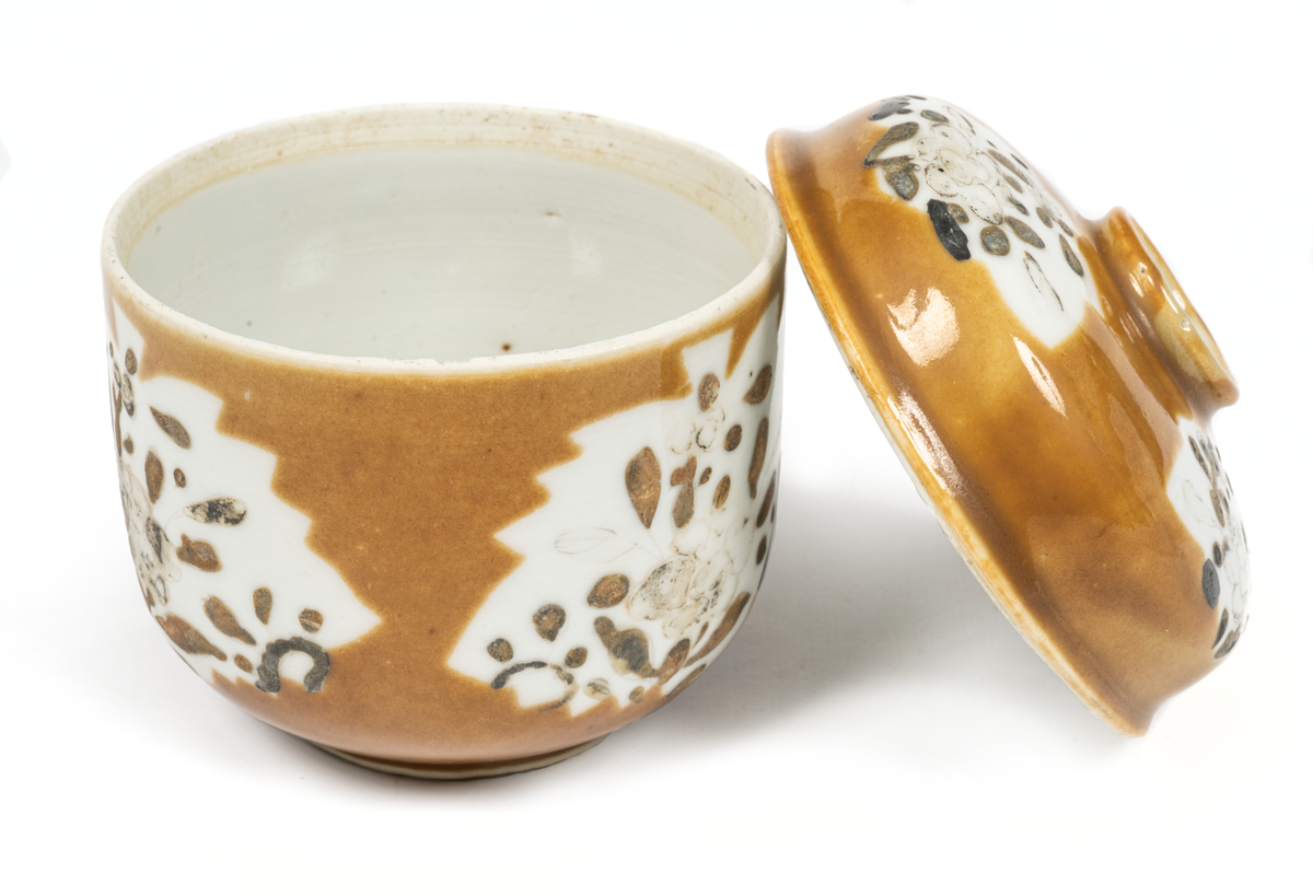 Bonbonier, bonbonjär. Skål med lock av ostindiskt porslin. Glaserad med brungul färg, vita bladformade fält med blomdekor i svart emaljfälrg. Enligt uppgift upptagen från den vid Hunnebådan sjunkna Ostindiefararens Göteborg".