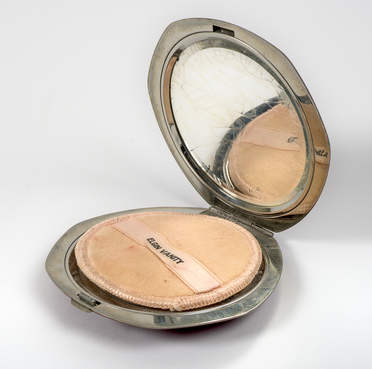 Oval puderdosa i metall med vinröd emaljerad yta. På ovansidan finns en metallplatta med silverfärgad text mot blå bakgrund: "1933, A Century of Progress, Chicago".

På insidan av locket sitter en spegel, medan botten har en rosa tyginsats för puder, märkt "ELGIN VANITY". Dosan stängs med en låsmekanism kopplad till en knapp.