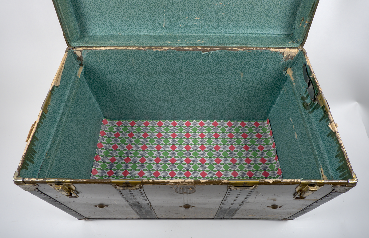 a) Rektangulär resekoffert med trästomme, utvändigt klädd i brunt papp och förstärkt med svartmålat konstläder. Kofferten är försedd med beslag och stötskydd av mässingspläterat stål. På vardera kortsida finns ett bärhandtag av kraftigt brunt läder. Koffertens framsida är försedd med låsanordningar bestående av två haspar samt i mitten ett ofullständigt lås, där låsdelen på kistans underdel saknas.

Invändigt har kofferten en uttagbar låda av papp, vilande på ribbor i kistans övre del. Insidan är klädd med grönt papper i geometriskt mönster. Bottendelen av lådan skyddas av ett smörpapper med blå prickar på vit botten. I kistans botten finns ett skyddande smörpapper med geometriska mönster i vitt, grönt och rött.

På vänster kortsida finns två stycken etiketter:

1. Swedish America Line.
2. Railway Express Agency (Attleboro, Massachusetts). Under denna etikett sitter fragment av en etikett i samma stil.

Se fotografi.

b) Pappersetikett med öljett, fäst i ståltråd: "Svenska.. Amerika. N: 936. Göteborgs Andra Bärarelag".