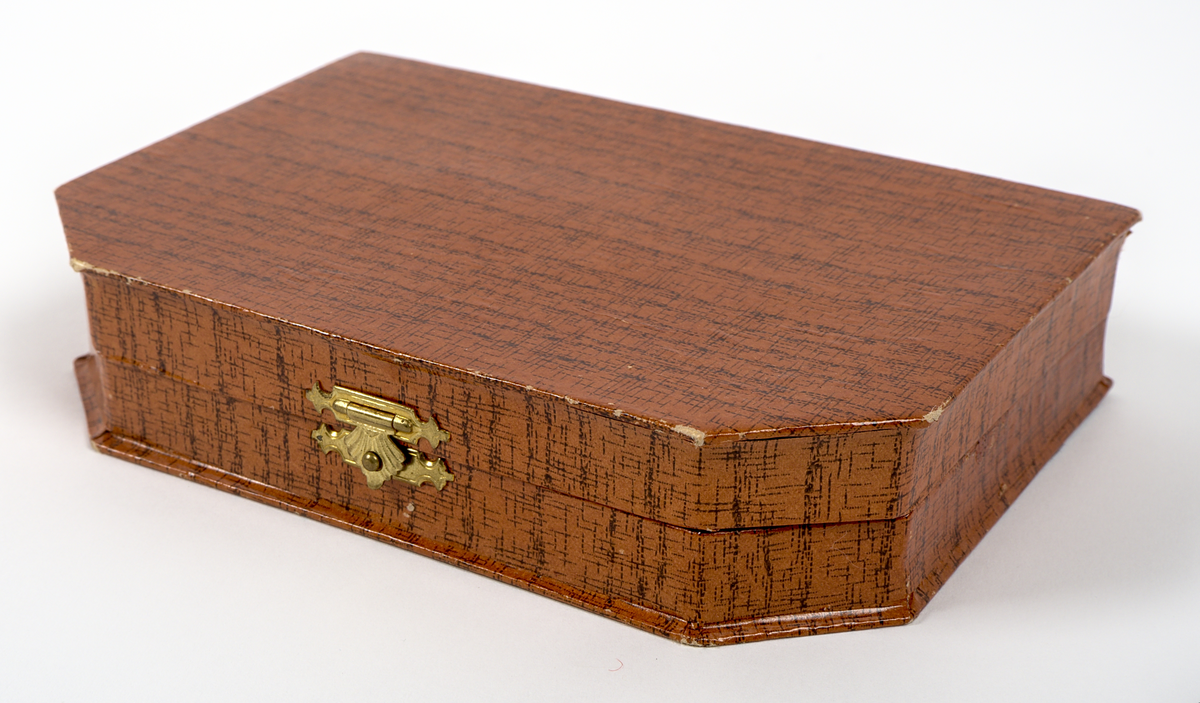 En uppsättning nagelvårdstillbehör med tillhörande etui.

a) Rektangulär ask av papp med yta i mahognyimitation. Framtill sitter en låsanordning i mässing, dekorerad med ett snäckformat beslag i art-deco stil. På insidan av locket finns en rombformad spegel, och på insidans botten en beige tyginsats kantad med ett flätat bomullsband.

b) Läppstift i cylindriskt format, inlindat i papper och aluminiumfolie. Längd: 50 mm.

c) Nagelpolerare med skaft av plast i sköldpaddsimitation. Nedre delen av mjukt material, klätt i läder. Längd: 62 mm. Bredd: 16 mm. Höjd 10 mm.

d) Nagelfil av papp med yta i mahognyimmitation. Sandpapper på undersidan. Längd 65 mm. Bredd 16 mm.

e) Nagelsticka av plast i sköldpaddsimitation. Längd: 90 mm.

f) Burk av plast. Tom på innehåll. Burken har troligtvis innehållet polermedel för nagelpoleraren.

De två tomrummen i asken visar att minst två delar saknas.