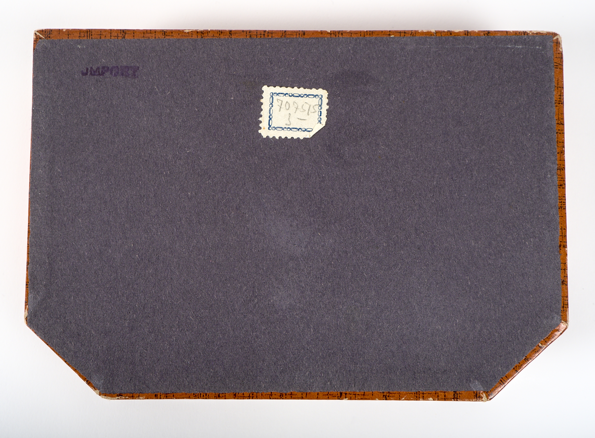 En uppsättning nagelvårdstillbehör med tillhörande etui.

a) Rektangulär ask av papp med yta i mahognyimitation. Framtill sitter en låsanordning i mässing, dekorerad med ett snäckformat beslag i art-deco stil. På insidan av locket finns en rombformad spegel, och på insidans botten en beige tyginsats kantad med ett flätat bomullsband.

b) Läppstift i cylindriskt format, inlindat i papper och aluminiumfolie. Längd: 50 mm.

c) Nagelpolerare med skaft av plast i sköldpaddsimitation. Nedre delen av mjukt material, klätt i läder. Längd: 62 mm. Bredd: 16 mm. Höjd 10 mm.

d) Nagelfil av papp med yta i mahognyimmitation. Sandpapper på undersidan. Längd 65 mm. Bredd 16 mm.

e) Nagelsticka av plast i sköldpaddsimitation. Längd: 90 mm.

f) Burk av plast. Tom på innehåll. Burken har troligtvis innehållet polermedel för nagelpoleraren.

De två tomrummen i asken visar att minst två delar saknas.