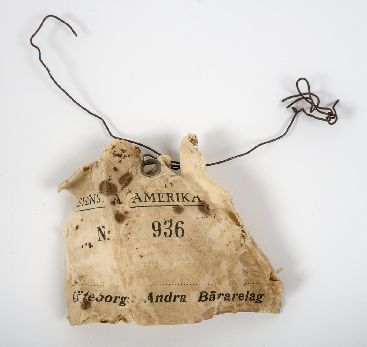 a) Rektangulär resekoffert med trästomme, utvändigt klädd i brunt papp och förstärkt med svartmålat konstläder. Kofferten är försedd med beslag och stötskydd av mässingspläterat stål. På vardera kortsida finns ett bärhandtag av kraftigt brunt läder. Koffertens framsida är försedd med låsanordningar bestående av två haspar samt i mitten ett ofullständigt lås, där låsdelen på kistans underdel saknas.

Invändigt har kofferten en uttagbar låda av papp, vilande på ribbor i kistans övre del. Insidan är klädd med grönt papper i geometriskt mönster. Bottendelen av lådan skyddas av ett smörpapper med blå prickar på vit botten. I kistans botten finns ett skyddande smörpapper med geometriska mönster i vitt, grönt och rött.

På vänster kortsida finns två stycken etiketter:

1. Swedish America Line.
2. Railway Express Agency (Attleboro, Massachusetts). Under denna etikett sitter fragment av en etikett i samma stil.

Se fotografi.

b) Pappersetikett med öljett, fäst i ståltråd: "Svenska.. Amerika. N: 936. Göteborgs Andra Bärarelag".