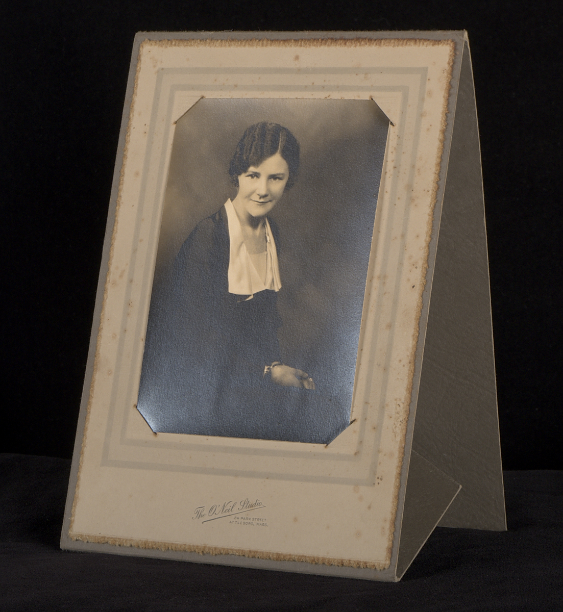 ​Fotografi monterat i ett etui av grå papp. Etuiet är självstagande när det vecklas ut. Under fotografiet finns en stämpel: "The O'Neil Studio. 24 Park Street. Attleboro, Mass", samt handskriven text: "December 1931".

Fotografiet föreställer en ung kvinna (Edith Torsson).