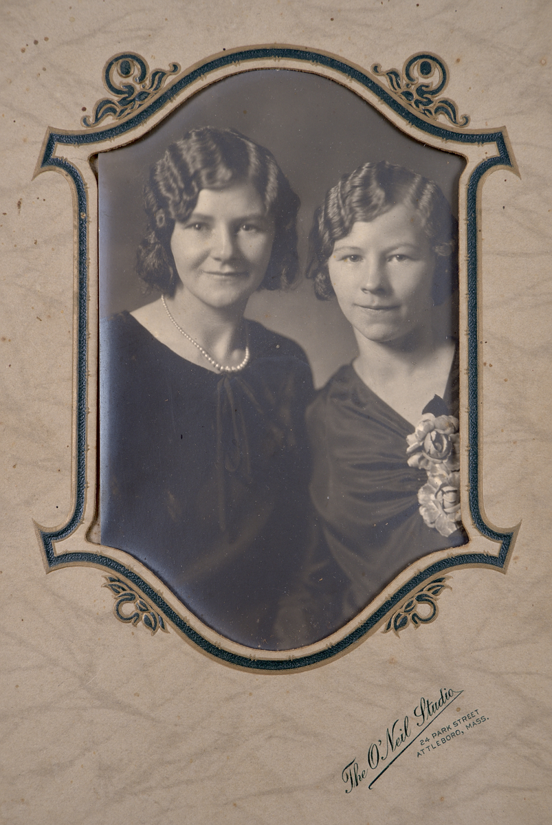 Fotografi monterat i etui av grå marmorerad papp. Etuiet är självstagande när det vecklas ut. Under fotografiet finns en stämpel: "The O'Neil Studio. 24 Park Street. Attleboro, Mass".

Fotografiet föreställer systrarna Edith (tv) och Sigrid (th) Torsson i finkläder.