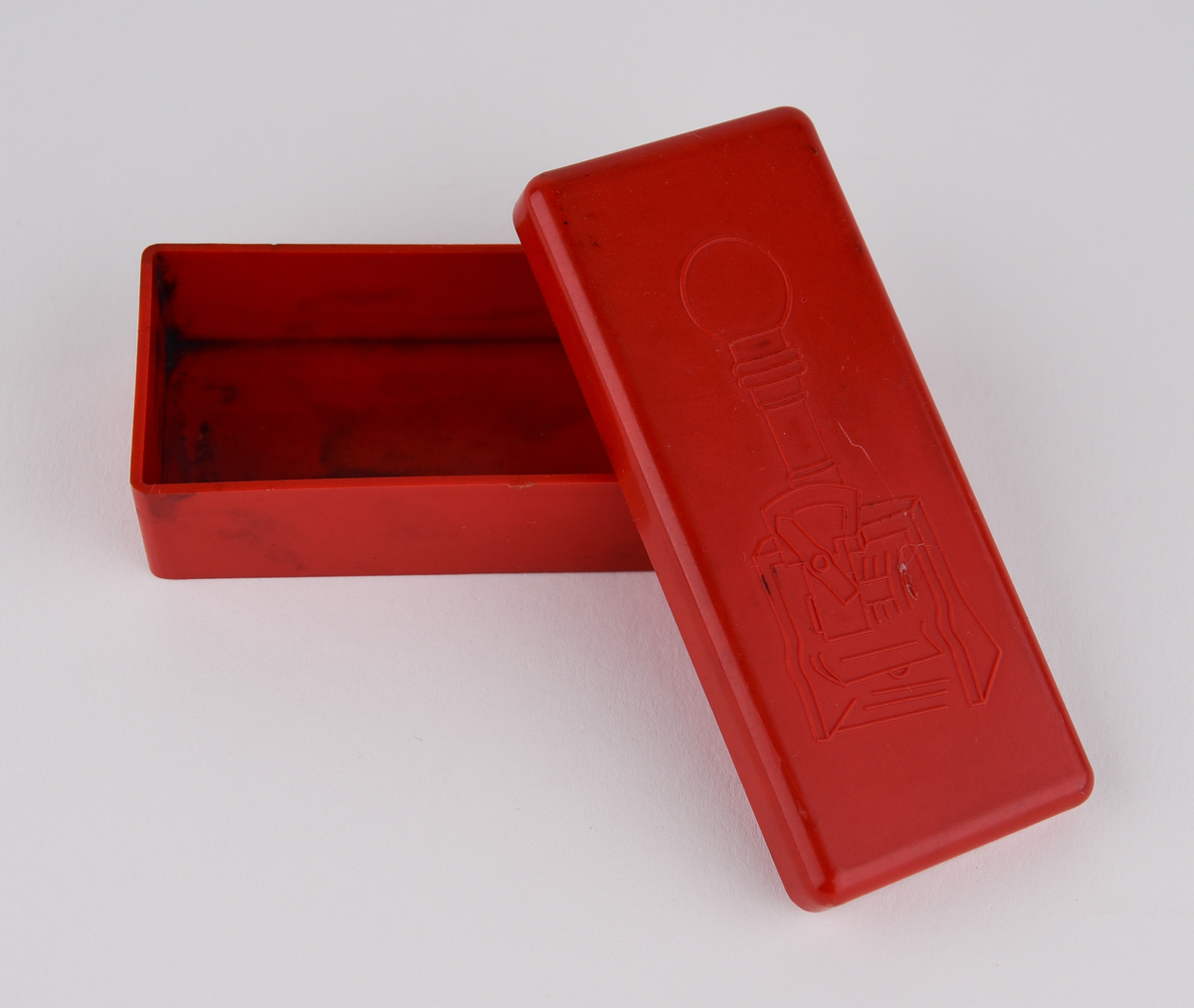 Stämpelfärg inlindad i papper i en röd ask av plast med en bild på en stämpel. Tysk text: "Schwartz, Metall Stempel Farbe". Består av tre delar: färgtub (Jvm23787-1-1), ask (Jvm23787-1-2) och lock till asken (Jvm23787-1-3).