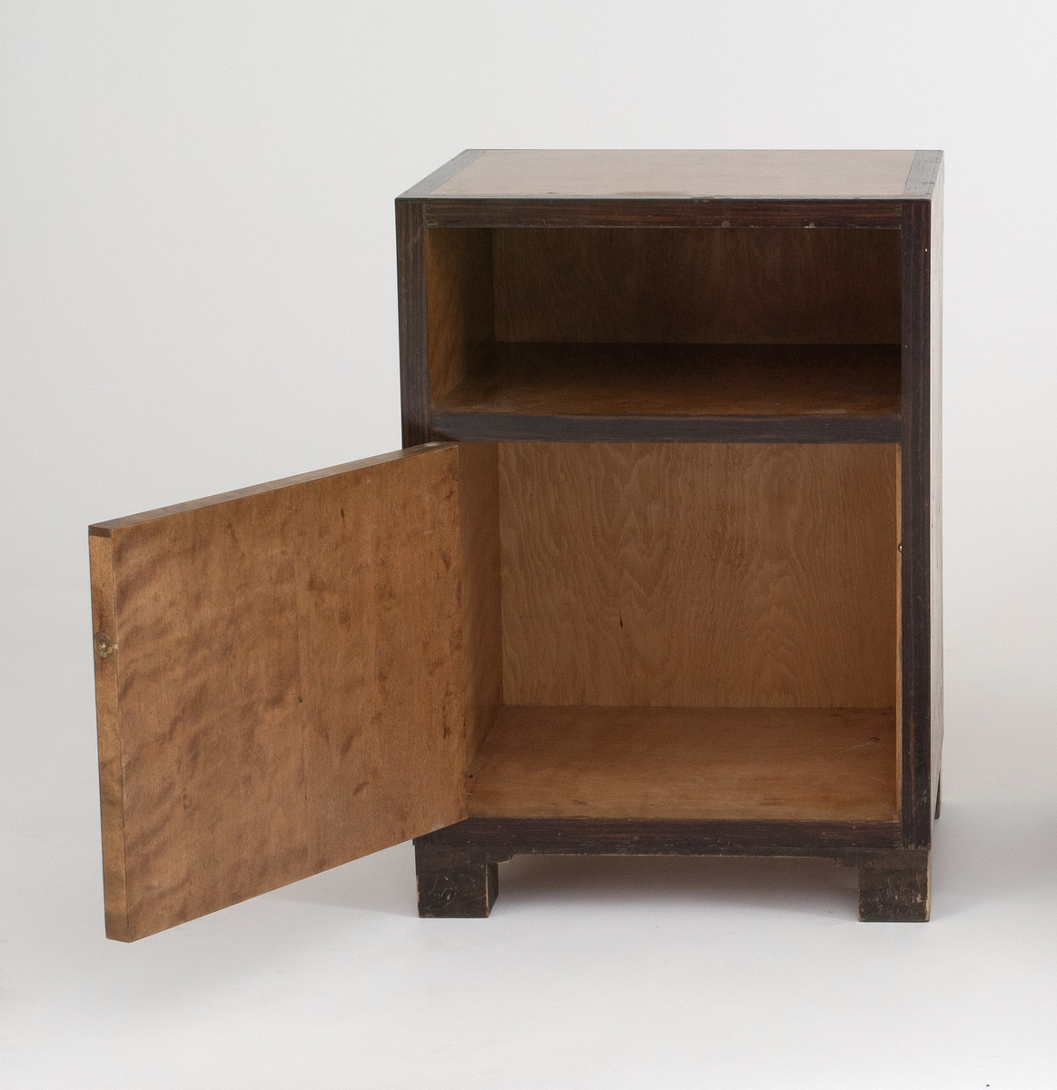 Rektangulært, rettlinjet nattbord i flammebjørkfinér på tre, med en ramme i mørkere finér. Nattbordet har en hylle samt et skap, på skapdøren en liten, rund knopp i øverste høyre hjørne som håndtak. Står på lave, firkantete fotstykker integrert i rammen.