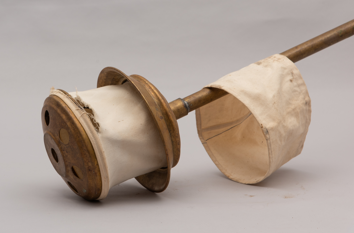 Vaskeredskap bestående av et messingrør til håndtak og et pumpehode i enden. Pumpehodet består av to messinglokk forbundet med et sluttet tekstilbånd, og en metallfjær inni som gir motstand. Nederste lokk har hull for å slippe inn vaskevannet. Godset er stemplet med Rena og initialene O.J.