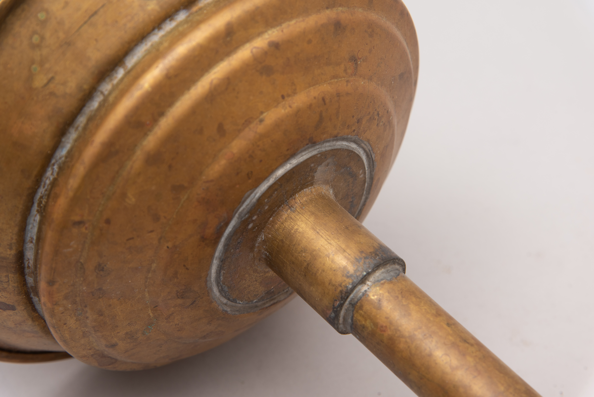 Vaskeredskap bestående av et messingrør til håndtak og et pumpehode i enden. Pumpehodet består av to messinglokk forbundet med et sluttet tekstilbånd, og en metallfjær inni som gir motstand. Nederste lokk har hull for å slippe inn vaskevannet. Godset er stemplet med Rena og initialene O.J.