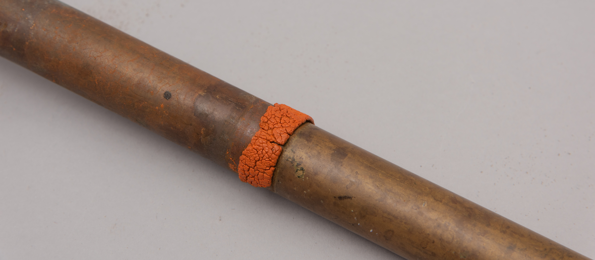 Vaskeredskap bestående av et messingrør til håndtak og et pumpehode i enden. Pumpehodet består av to messinglokk forbundet med et sluttet tekstilbånd, og en metallfjær inni som gir motstand. Nederste lokk har hull for å slippe inn vaskevannet. Godset er stemplet med Rena og initialene O.J.