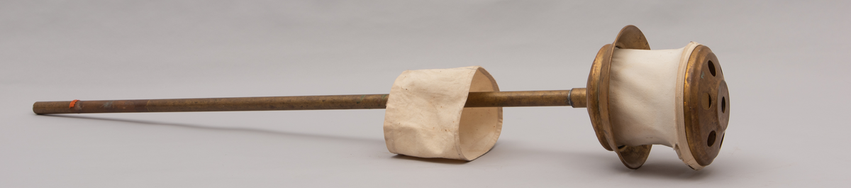 Vaskeredskap bestående av et messingrør til håndtak og et pumpehode i enden. Pumpehodet består av to messinglokk forbundet med et sluttet tekstilbånd, og en metallfjær inni som gir motstand. Nederste lokk har hull for å slippe inn vaskevannet. Godset er stemplet med Rena og initialene O.J.