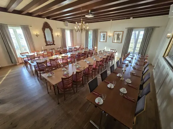 Fire langbord dekket med kopp, skål, serviett og glass til mer enn 60 personer, store vinduer med lyse gardiner, rokokkospeil og lysekrone.