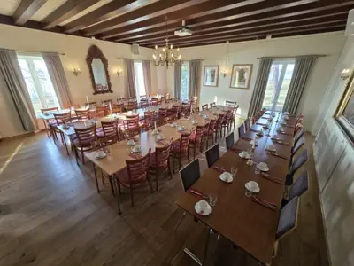 Fire langbord dekket med kopp, skål, serviett og glass til mer enn 60 personer, store vinduer med lyse gardiner, rokokkospeil og lysekrone.