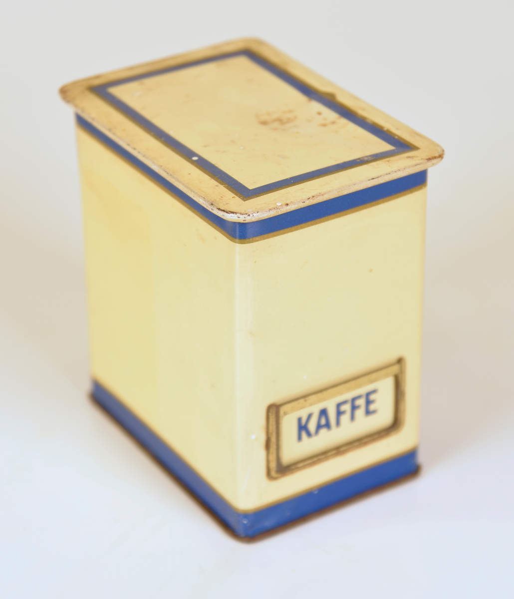 Gula ålåtburkar med blå dekor. Etiketthållare , två med KAFFE tryckt på burken, en med vit plastetikett med text "SOCKER" i svart och en med etikett med "KAKAO".  Det kan vara så att när man köpt kaffe har man fått det i burken samt lösa etiketter för att återanvända burken till annat när kaffet var slut.

Från Arne Ekströms handelsmuseum.