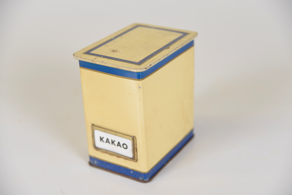 Gula ålåtburkar med blå dekor. Etiketthållare , två med KAFFE tryckt på burken, en med vit plastetikett med text "SOCKER" i svart och en med etikett med "KAKAO".  Det kan vara så att när man köpt kaffe har man fått det i burken samt lösa etiketter för att återanvända burken till annat när kaffet var slut.

Från Arne Ekströms handelsmuseum.