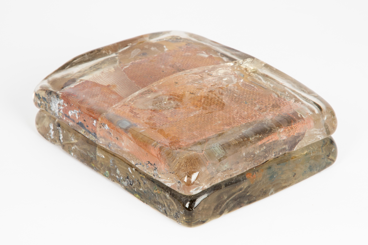 Glassform i klart glass med innlagt dekor. Består av to rektangulære flater som er smeltet sammen med et kobbernett og en gullfarget plate mellom.