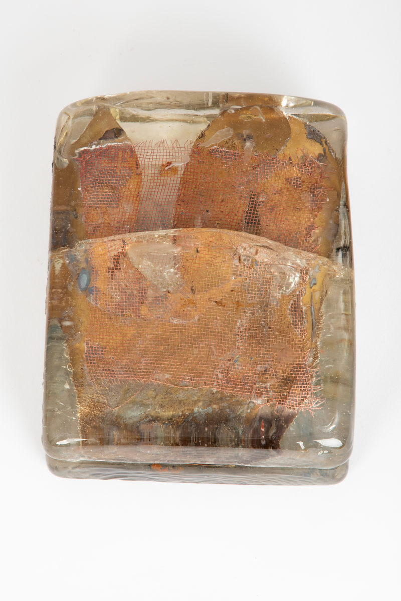 Glassform i klart glass med innlagt dekor. Består av to rektangulære flater som er smeltet sammen med et kobbernett og en gullfarget plate mellom.