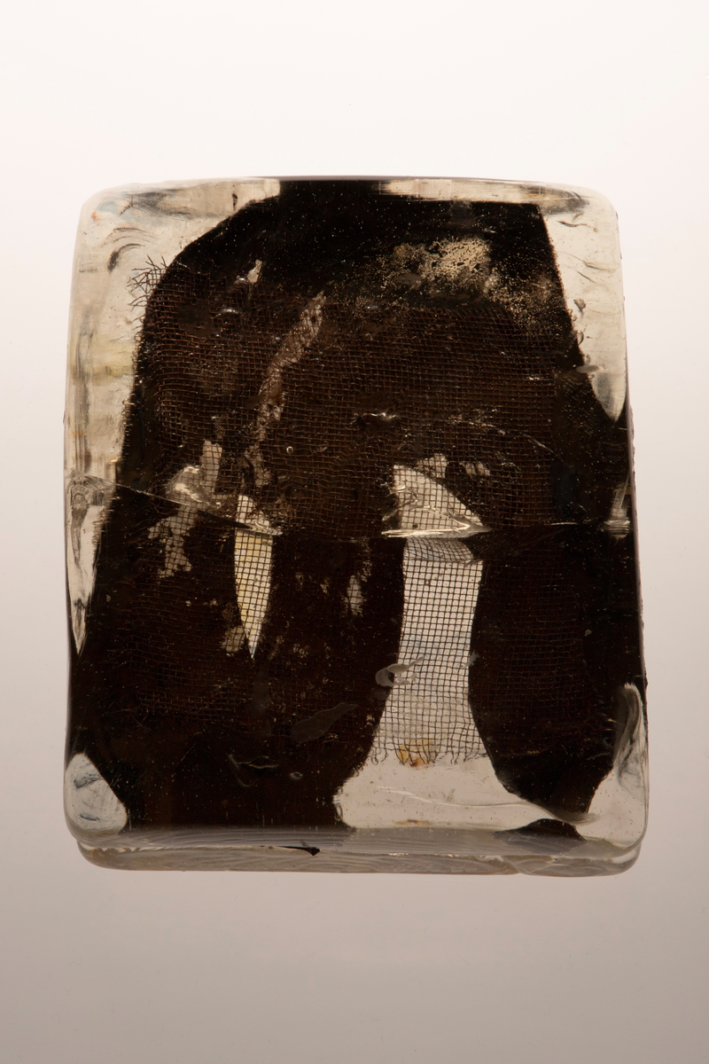 Glassform i klart glass med innlagt dekor. Består av to rektangulære flater som er smeltet sammen med et kobbernett og en gullfarget plate mellom.