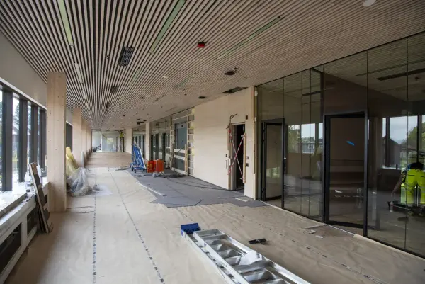 Tak med langsgående trespiler, glv dekket med gråpapir, vegger i glass og tre.