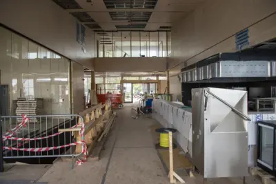 Til høyre: restaurantkjøkken i stål monteres. Rett fram: hovedinngangen med glassgang i kontorfløyen over. Til venstre: nedgang til garderobe, sikret med provisorisk gjerde.