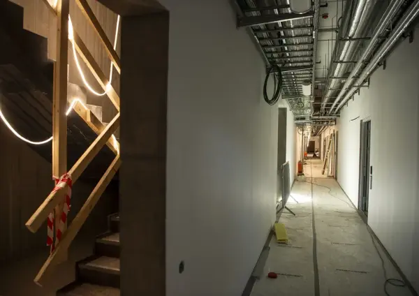 Til venstre i bildet en støpt trapp med ledlysstriper hengende, til høyre en lang korridor med rør i taket.