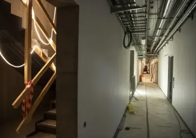 Til venstre i bildet en støpt trapp med ledlysstriper hengende, til høyre en lang korridor med rør i taket.