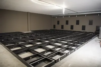 Lysegrå vegger, den ene med mørkere firkanter i tannmønster. På golvet ligger bunnrammene til arkivreoler som et mørkt firkantmønster.