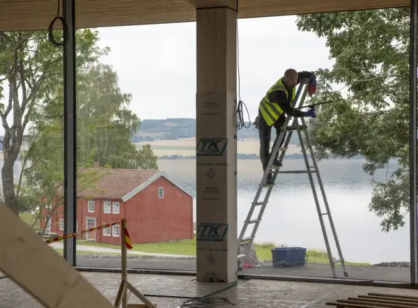 En mann står på høy gardintrapp og pusser vinduer i det regionale historiesenteret, Mjøsa og Løtenbygningen ses utenfor.