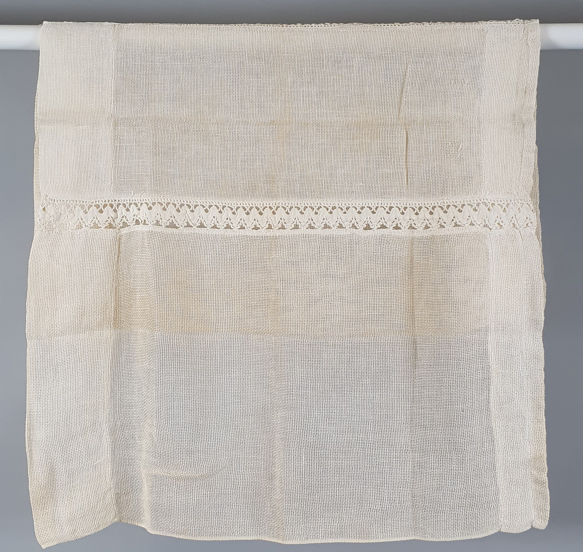 Hvit (gulnet) gardin med 2 innsydde blondebånd på midten.