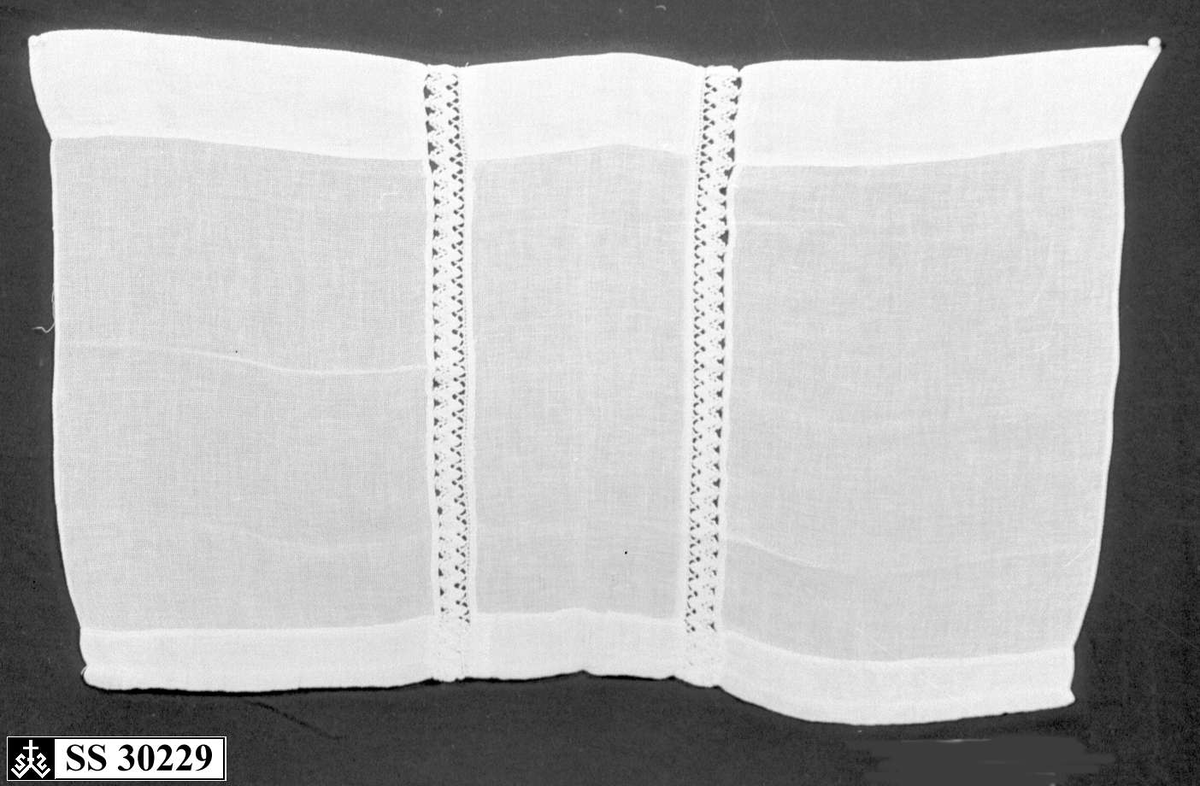 Hvit (gulnet) gardin med 2 innsydde blondebånd på midten.