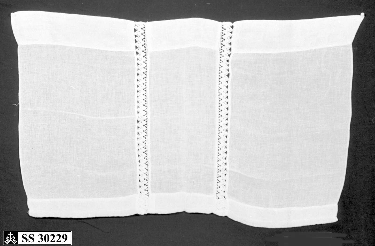 Hvit (gulnet) gardin med 2 innsydde blondebånd på midten.