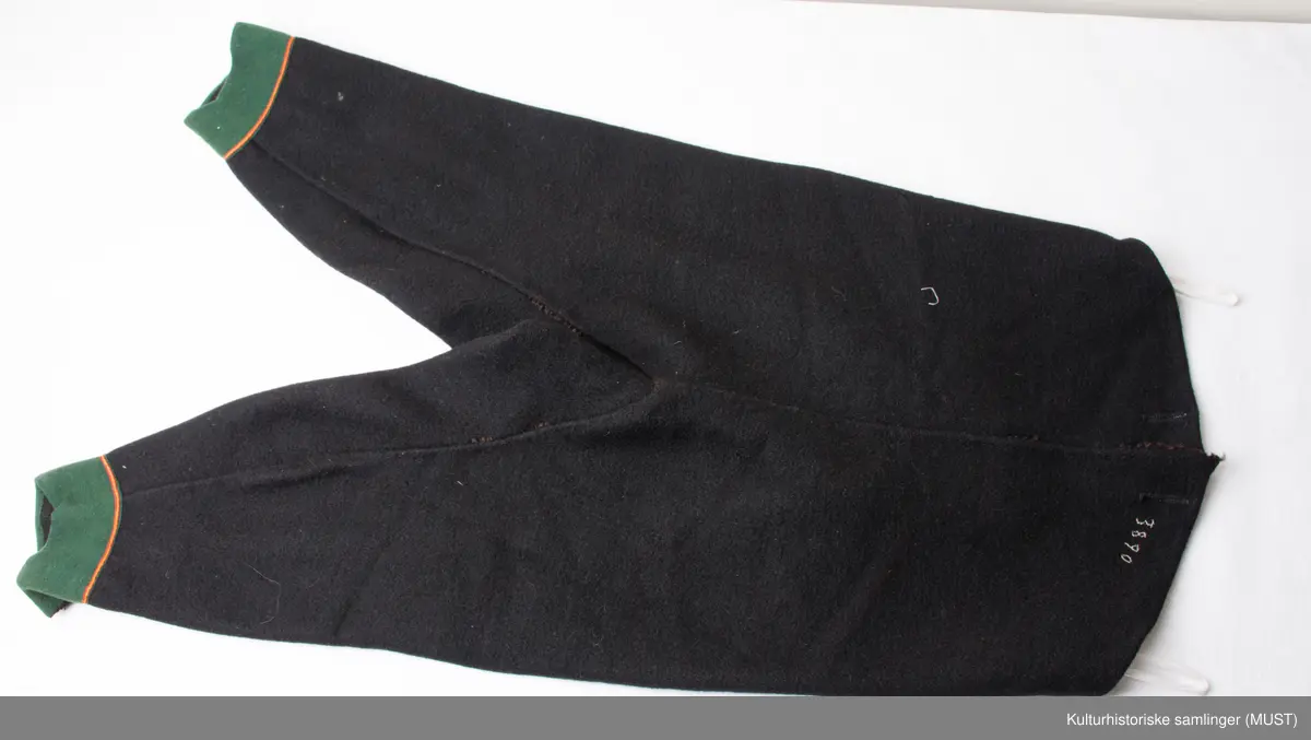 Bukse har fire hovedstykker i vadmel. Midtsøm framme og søm fra låket har innlagt grønn titte kant.
Den indre sømmen på bukse beinet går et stykke opp i baken før den møter baksømmen.
Bukse har smalt låk, belagt med grønnt klede med brodere og åtte knapphull og tre knapper. Tre knapper mangler. En kuleknapp i messing. To knapper i messing og grønn glass.
Lommeklaff oppstående (høyre side) belagt med grønnt klede med broderi. Grønn titte kant nede.
Lommefor lerret et firkantet stykke på sydd som lomme.
Nede, buksebein smale nederest bredde. Kantet med grønnt klede og opp splitt. Fire knapphull, fire messing kuleknapp og ullbroderi.