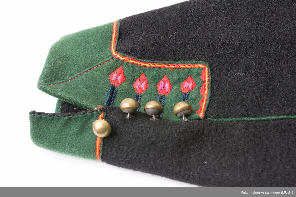 Bukse har fire hovedstykker i vadmel. Midtsøm framme og søm fra låket har innlagt grønn titte kant.
Den indre sømmen på bukse beinet går et stykke opp i baken før den møter baksømmen.
Bukse har smalt låk, belagt med grønnt klede med brodere og åtte knapphull og tre knapper. Tre knapper mangler. En kuleknapp i messing. To knapper i messing og grønn glass.
Lommeklaff oppstående (høyre side) belagt med grønnt klede med broderi. Grønn titte kant nede.
Lommefor lerret et firkantet stykke på sydd som lomme.
Nede, buksebein smale nederest bredde. Kantet med grønnt klede og opp splitt. Fire knapphull, fire messing kuleknapp og ullbroderi.