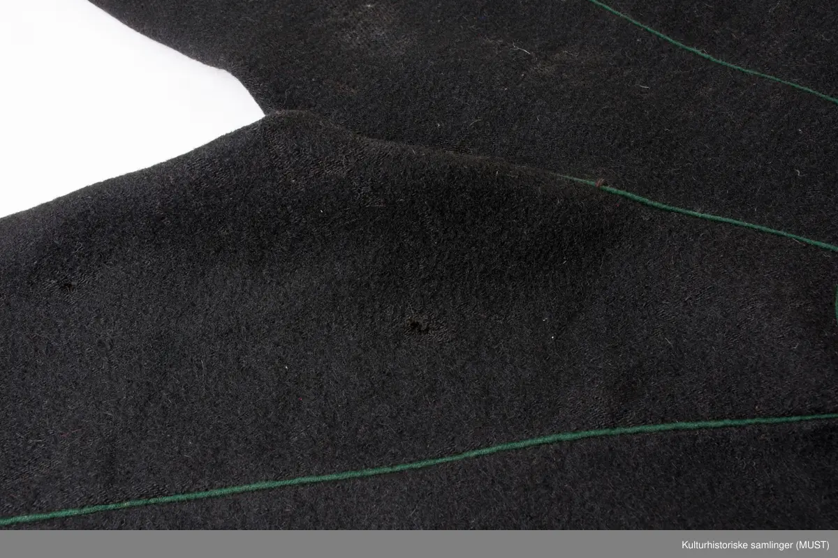 Bukse har fire hovedstykker i vadmel. Midtsøm framme og søm fra låket har innlagt grønn titte kant.
Den indre sømmen på bukse beinet går et stykke opp i baken før den møter baksømmen.
Bukse har smalt låk, belagt med grønnt klede med brodere og åtte knapphull og tre knapper. Tre knapper mangler. En kuleknapp i messing. To knapper i messing og grønn glass.
Lommeklaff oppstående (høyre side) belagt med grønnt klede med broderi. Grønn titte kant nede.
Lommefor lerret et firkantet stykke på sydd som lomme.
Nede, buksebein smale nederest bredde. Kantet med grønnt klede og opp splitt. Fire knapphull, fire messing kuleknapp og ullbroderi.