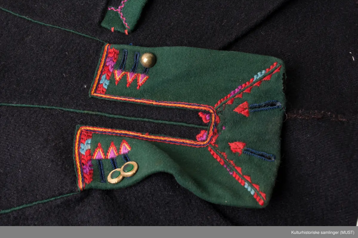 Bukse har fire hovedstykker i vadmel. Midtsøm framme og søm fra låket har innlagt grønn titte kant.
Den indre sømmen på bukse beinet går et stykke opp i baken før den møter baksømmen.
Bukse har smalt låk, belagt med grønnt klede med brodere og åtte knapphull og tre knapper. Tre knapper mangler. En kuleknapp i messing. To knapper i messing og grønn glass.
Lommeklaff oppstående (høyre side) belagt med grønnt klede med broderi. Grønn titte kant nede.
Lommefor lerret et firkantet stykke på sydd som lomme.
Nede, buksebein smale nederest bredde. Kantet med grønnt klede og opp splitt. Fire knapphull, fire messing kuleknapp og ullbroderi.