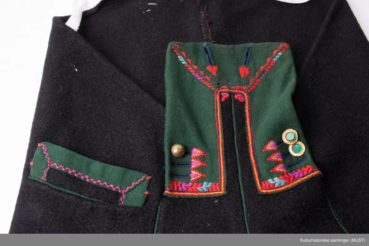 Bukse har fire hovedstykker i vadmel. Midtsøm framme og søm fra låket har innlagt grønn titte kant.
Den indre sømmen på bukse beinet går et stykke opp i baken før den møter baksømmen.
Bukse har smalt låk, belagt med grønnt klede med brodere og åtte knapphull og tre knapper. Tre knapper mangler. En kuleknapp i messing. To knapper i messing og grønn glass.
Lommeklaff oppstående (høyre side) belagt med grønnt klede med broderi. Grønn titte kant nede.
Lommefor lerret et firkantet stykke på sydd som lomme.
Nede, buksebein smale nederest bredde. Kantet med grønnt klede og opp splitt. Fire knapphull, fire messing kuleknapp og ullbroderi.